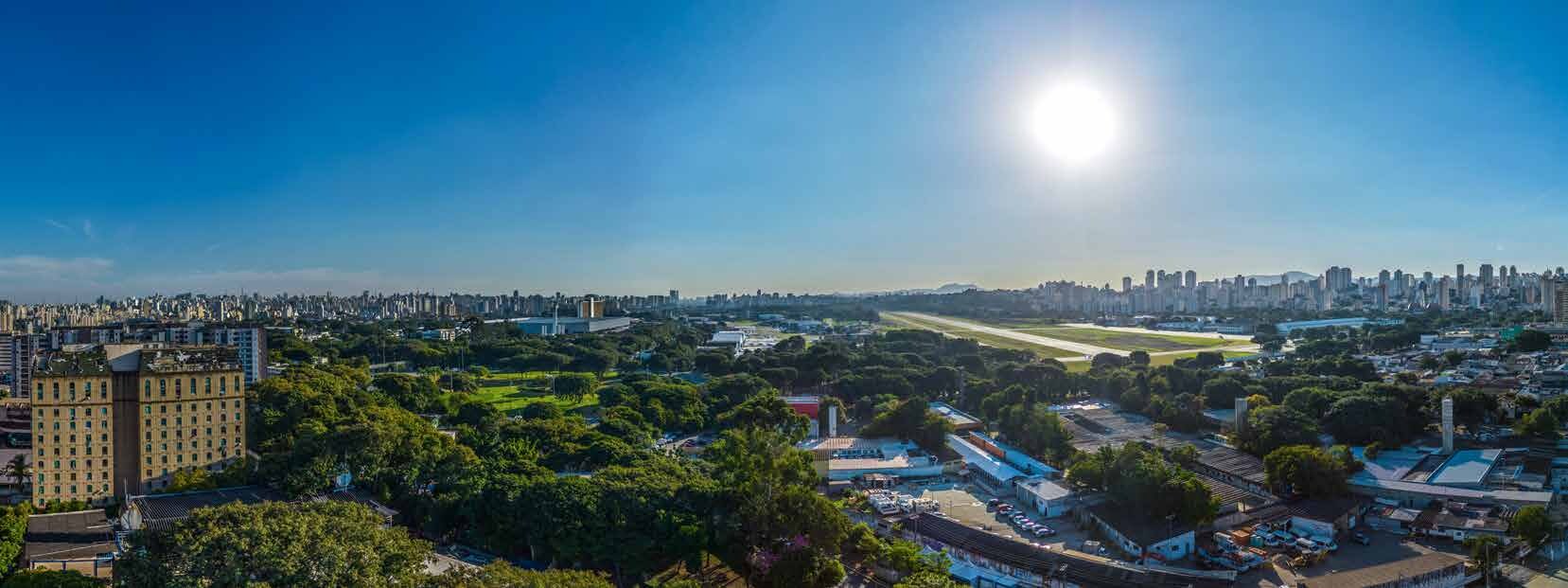 Vista real captada por drone na altura do 15º pavimento, mostrando o Campo de Marte e o horizonte de São Paulo